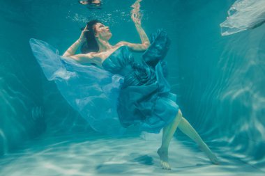 güzel model kız su altında mavi elbiseli yüzüyor ve rahatlama ve stres eksikliği sahiptir