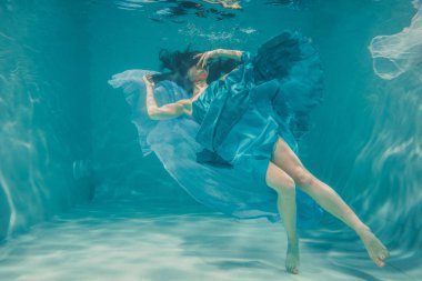 uzun siyah saçlı güzel model kız su altında mavi elbise ve rahatlama ve stres eksikliği sahiptir akşam yüzer