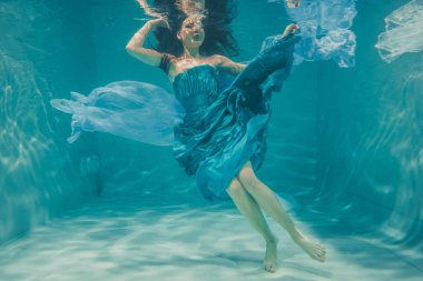 uzun siyah saçlı güzel model kız su altında mavi elbise ve rahatlama ve stres eksikliği sahiptir akşam yüzer