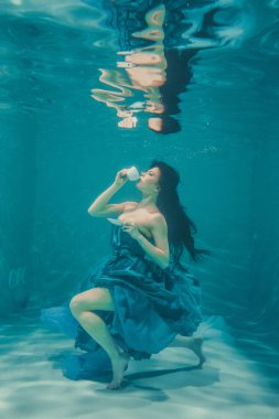 eğleniyor ve meditatively su altında bir elbise içinde yüzme sırasında kahvaltı için yatıştırıcı çay içme kız