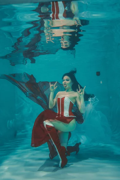 beautiful sexy girl swimming underwater in sporty style red and white fetish corset and over knee thigh high boots with heels