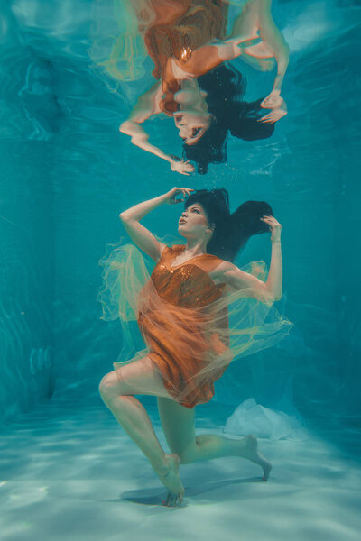 beautiful model girl swims underwater in orange dress and enjoys relaxation and lack of stress