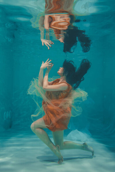 beautiful model girl swims underwater in orange dress and enjoys relaxation and lack of stress