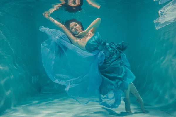 美丽的模特女孩与长黑头发游泳水下晚上蓝色礼服 享受放松和缺乏压力 — 图库照片