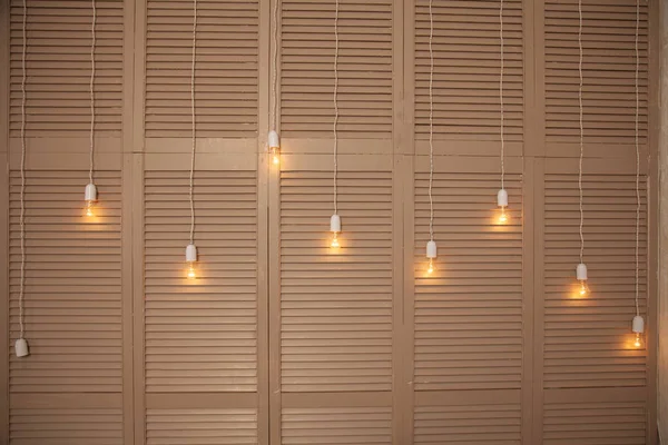 在房间里的米色木壁橱的背景上挂着长长的电线上的灯泡 — 图库照片