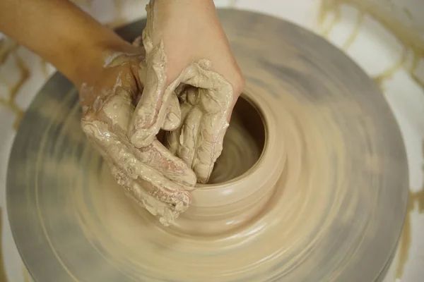 woman makes a jug with dirty arms on a Potter's wheel from raw wet clay