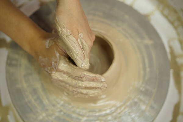 Женщина делает кувшин с грязными руками на гончарном круге из сырой влажной глины
