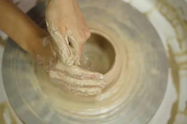 woman makes a jug with dirty arms on a Potter\'s wheel from raw wet clay