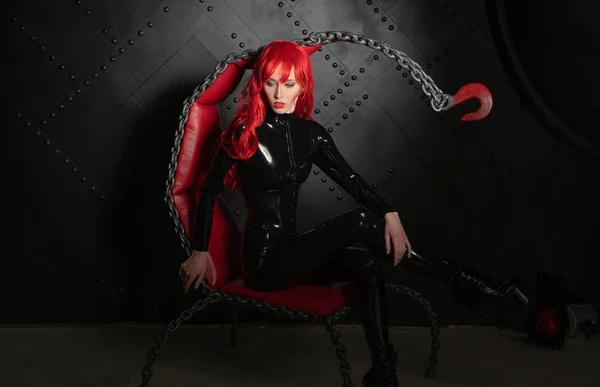 サドマゾヒズムのスタイルのチェーンから椅子に黒い Bdsm ラテックス服でポーズをとって赤い髪の危険な残酷なフェチ少女 — ストック写真