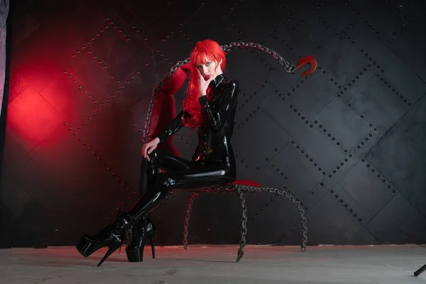 危险的残酷恋物癖女孩与红头发摆姿势黑色的 Bdsm 乳胶衣服在椅子上的链在虐待狂的风格 — 图库照片
