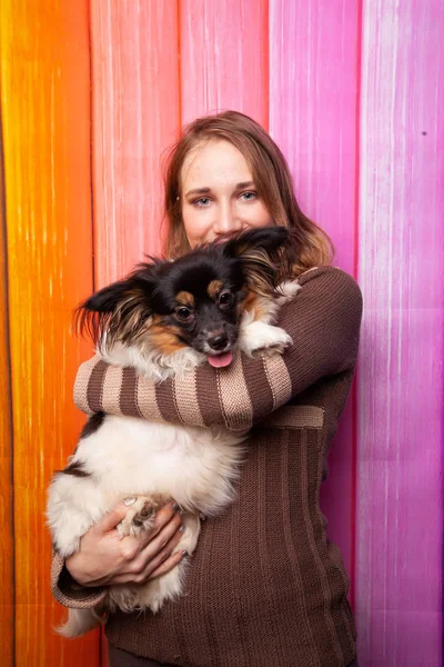 美丽的高加索女孩摆姿势在棕色毛衣与狗在她的怀里 — 图库照片