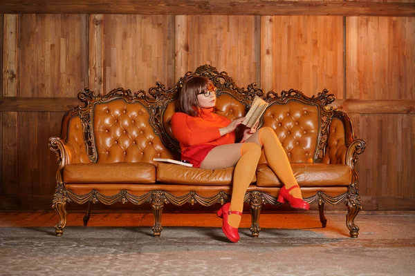 cute girl with glasses in orange clothes is a good student and a nerd, she like reading book on the sofa at home alone