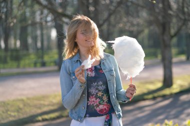 Beyaz kız büyüleyici bir kot ceket baharda Park içeri girer ve pembe pamuk şeker, sabah güneş ışığı gülümsüyor yiyor