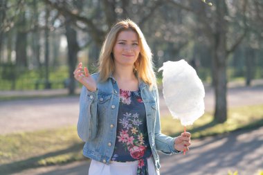 Beyaz kız büyüleyici bir kot ceket baharda Park içeri girer ve pembe pamuk şeker, sabah güneş ışığı gülümsüyor yiyor