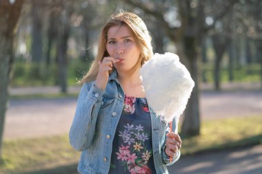 Beyaz kız büyüleyici bir kot ceket baharda Park içeri girer ve pembe pamuk şeker, sabah güneş ışığı gülümsüyor yiyor