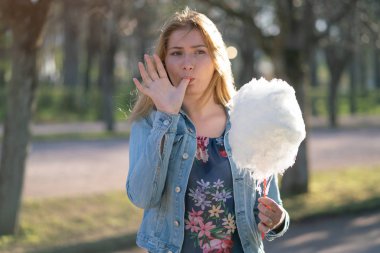 Beyaz kız büyüleyici bir kot ceket baharda Park içeri girer ve pembe pamuk şeker, sabah güneş ışığı gülümsüyor yiyor