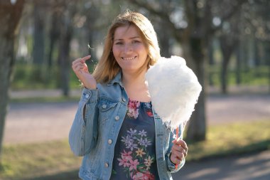 Beyaz kız büyüleyici bir kot ceket baharda Park içeri girer ve pembe pamuk şeker, sabah güneş ışığı gülümsüyor yiyor