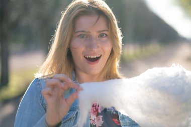 Beyaz kız büyüleyici bir kot ceket baharda Park içeri girer ve pembe pamuk şeker, sabah güneş ışığı gülümsüyor yiyor