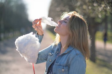 Beyaz kız büyüleyici bir kot ceket baharda Park içeri girer ve pembe pamuk şeker, sabah güneş ışığı gülümsüyor yiyor