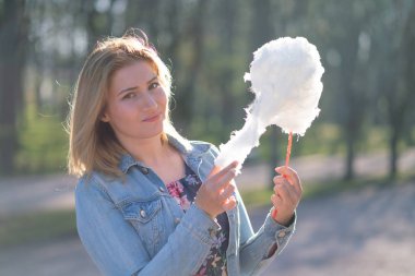 Beyaz kız büyüleyici bir kot ceket baharda Park içeri girer ve pembe pamuk şeker, sabah güneş ışığı gülümsüyor yiyor