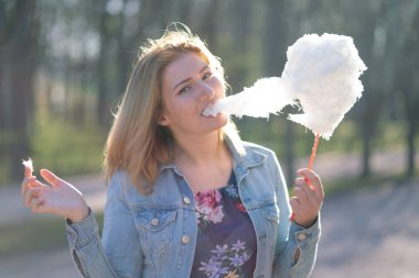 Beyaz kız büyüleyici bir kot ceket baharda Park içeri girer ve pembe pamuk şeker, sabah güneş ışığı gülümsüyor yiyor