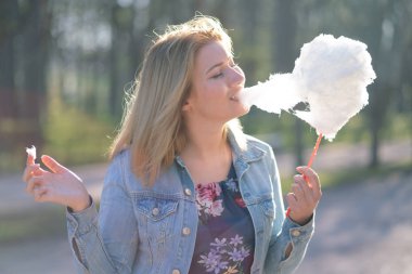 Beyaz kız büyüleyici bir kot ceket baharda Park içeri girer ve pembe pamuk şeker, sabah güneş ışığı gülümsüyor yiyor