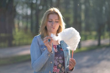 Beyaz kız büyüleyici bir kot ceket baharda Park içeri girer ve pembe pamuk şeker, sabah güneş ışığı gülümsüyor yiyor