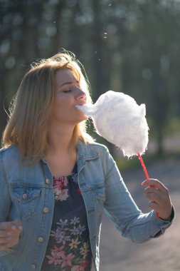 Beyaz kız büyüleyici bir kot ceket baharda Park içeri girer ve pembe pamuk şeker, sabah güneş ışığı gülümsüyor yiyor