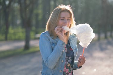 Beyaz kız büyüleyici bir kot ceket baharda Park içeri girer ve pembe pamuk şeker, sabah güneş ışığı gülümsüyor yiyor