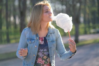 Beyaz kız büyüleyici bir kot ceket baharda Park içeri girer ve pembe pamuk şeker, sabah güneş ışığı gülümsüyor yiyor