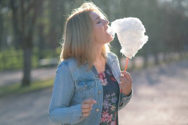 Beyaz kız büyüleyici bir kot ceket baharda Park içeri girer ve pembe pamuk şeker, sabah güneş ışığı gülümsüyor yiyor