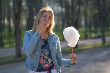 Beyaz kız büyüleyici bir kot ceket baharda Park içeri girer ve pembe pamuk şeker, sabah güneş ışığı gülümsüyor yiyor
