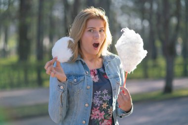 Beyaz kız büyüleyici bir kot ceket baharda Park içeri girer ve pembe pamuk şeker, sabah güneş ışığı gülümsüyor yiyor