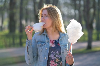 Beyaz kız büyüleyici bir kot ceket baharda Park içeri girer ve pembe pamuk şeker, sabah güneş ışığı gülümsüyor yiyor