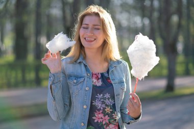 Beyaz kız büyüleyici bir kot ceket baharda Park içeri girer ve pembe pamuk şeker, sabah güneş ışığı gülümsüyor yiyor