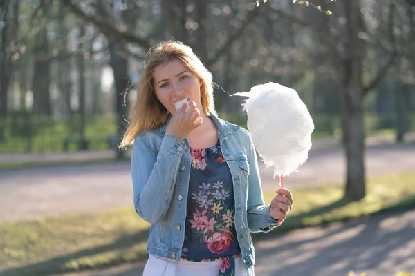 Beyaz kız büyüleyici bir kot ceket baharda Park içeri girer ve pembe pamuk şeker, sabah güneş ışığı gülümsüyor yiyor