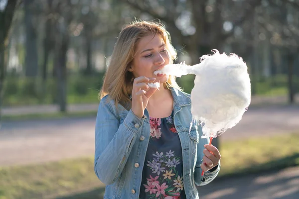 Beyaz kız büyüleyici bir kot ceket baharda Park içeri girer ve pembe pamuk şeker, sabah güneş ışığı gülümsüyor yiyor
