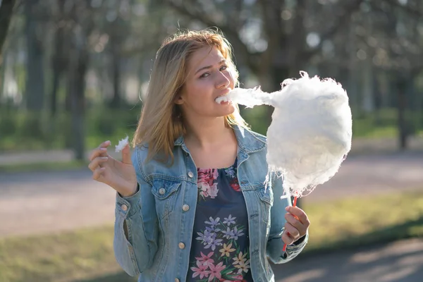 Beyaz kız büyüleyici bir kot ceket baharda Park içeri girer ve pembe pamuk şeker, sabah güneş ışığı gülümsüyor yiyor