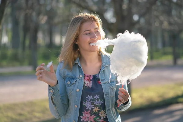 Beyaz kız büyüleyici bir kot ceket baharda Park içeri girer ve pembe pamuk şeker, sabah güneş ışığı gülümsüyor yiyor
