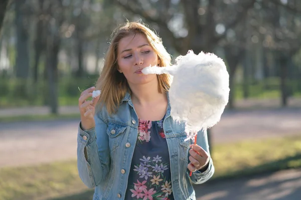 Beyaz kız büyüleyici bir kot ceket baharda Park içeri girer ve pembe pamuk şeker, sabah güneş ışığı gülümsüyor yiyor
