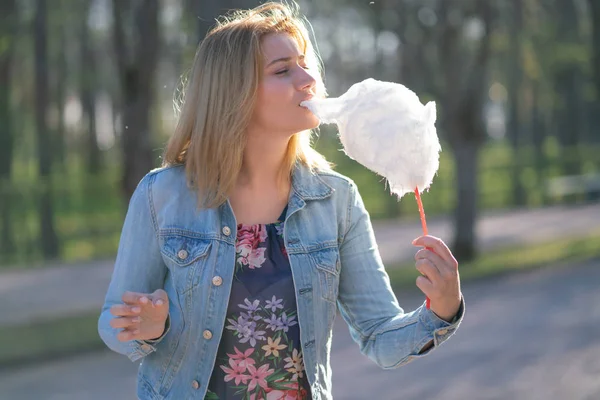 Beyaz kız büyüleyici bir kot ceket baharda Park içeri girer ve pembe pamuk şeker, sabah güneş ışığı gülümsüyor yiyor