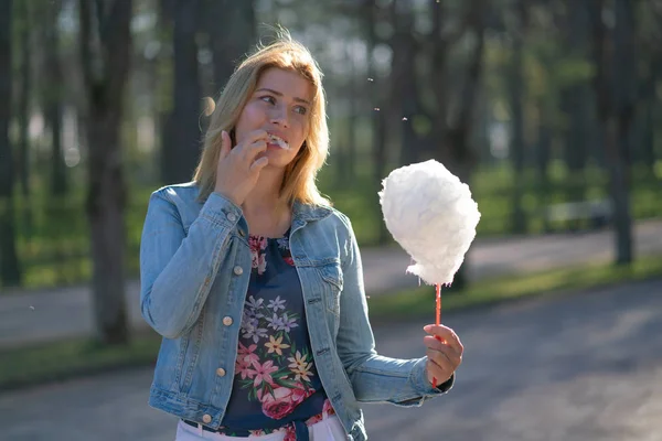 Beyaz kız büyüleyici bir kot ceket baharda Park içeri girer ve pembe pamuk şeker, sabah güneş ışığı gülümsüyor yiyor