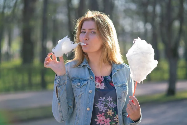 Beyaz kız büyüleyici bir kot ceket baharda Park içeri girer ve pembe pamuk şeker, sabah güneş ışığı gülümsüyor yiyor