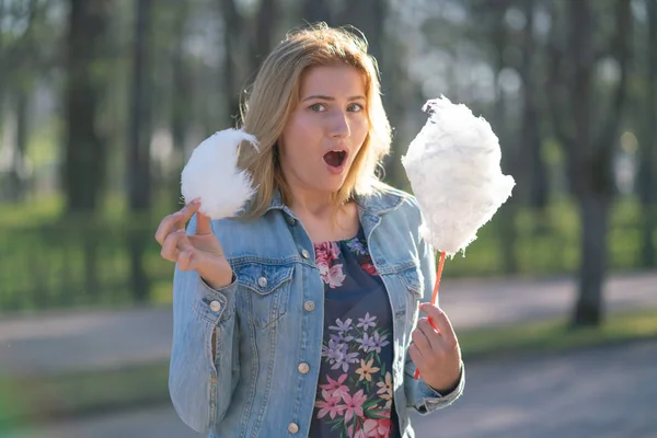 Beyaz kız büyüleyici bir kot ceket baharda Park içeri girer ve pembe pamuk şeker, sabah güneş ışığı gülümsüyor yiyor