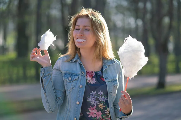 Beyaz kız büyüleyici bir kot ceket baharda Park içeri girer ve pembe pamuk şeker, sabah güneş ışığı gülümsüyor yiyor