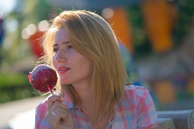 yeme ve kırmızı karamelli elma Park güneşli bir günde ısırma genç ve güzel kadın