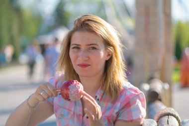 yeme ve kırmızı karamelli elma Park güneşli bir günde ısırma genç ve güzel kadın