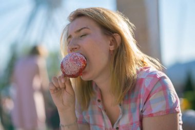 yeme ve kırmızı karamelli elma Park güneşli bir günde ısırma genç ve güzel kadın