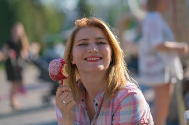 yeme ve kırmızı karamelli elma Park güneşli bir günde ısırma genç ve güzel kadın