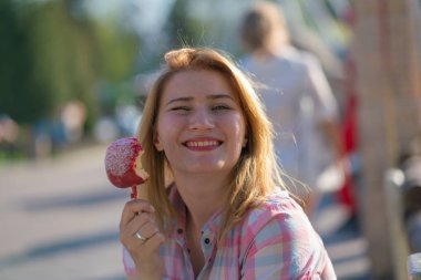 yeme ve kırmızı karamelli elma Park güneşli bir günde ısırma genç ve güzel kadın